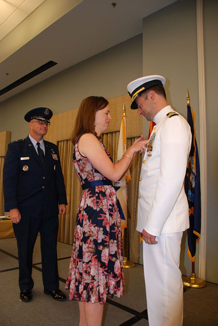 Joy Klemm places the Defense Logistics Agency command pin on her husband, Navy Cmdr. Keith Klemm, during a DLA Aviation – Cherry Point change of command ceremony June 16, 2017 at Marine Corps Air Station Cherry Point, North Carolina. The ceremony was officiated by DLA Aviation Commander Air Force Brig. Gen. Allan Day (left).