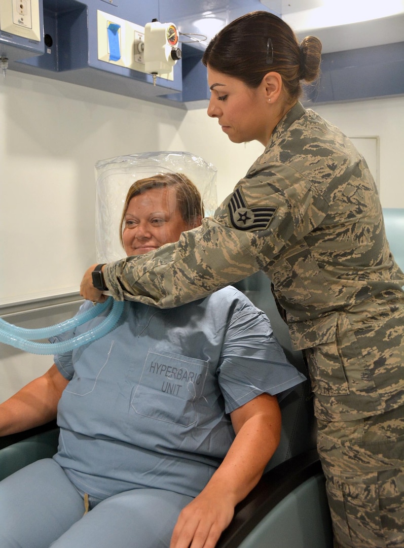 Air Force Staff Sgt. Maribel Cortez, certified hyperbaric technician, places the oxygen hood on Christen Hesser to demonstrate how a patient would receive oxygen therapy in the multi-person chamber at the new Undersea & Hyperbaric Medicine Clinic at Brooke Army Medical Center at Joint Base San Antonio-Fort Sam Houston June 13. If the patient is not comfortable with the hood, they can also wear a mask to receive their treatment. 