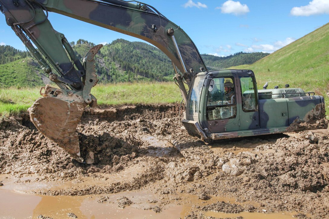 South Dakota Army National Guard Sgt. Justin Symmonds uses a hydraulic excavator to dig a hole to assist with water drainage in support of Golden Coyote, Lead, S.D., June 14, 2017. Symmonds is assigned to the 842nd Engineer Company. Golden Coyote enables commanders to focus on mission essential task requirements, warrior tasks and drills. Army photo by Spc. Jeffery Harris