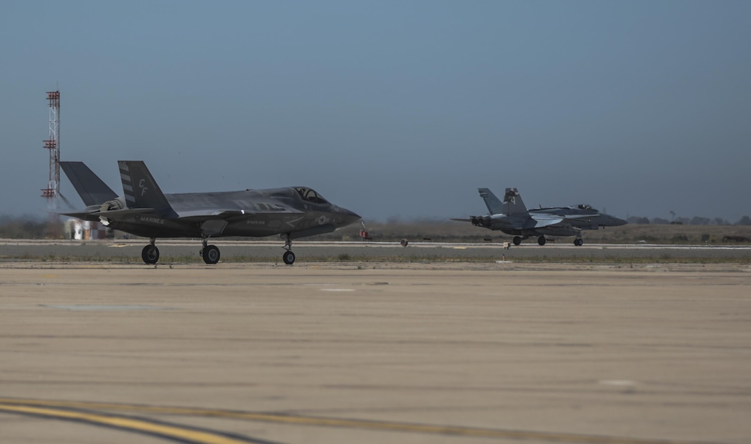An F-35B Lightning II with Marine Fighter Attack Squadron 211 taxis on the flightline while an F/A-18 Hornet takes off during the Marine Division Tactics Course at Marine Corps Air Station Miramar, Calif., June 16. This course gives pilots air-to-air combat experience and the tools to train Marines in their squadrons on the latest tactics. (U.S. Marine Corps photo by Sgt. Kimberlyn Adams/Released)