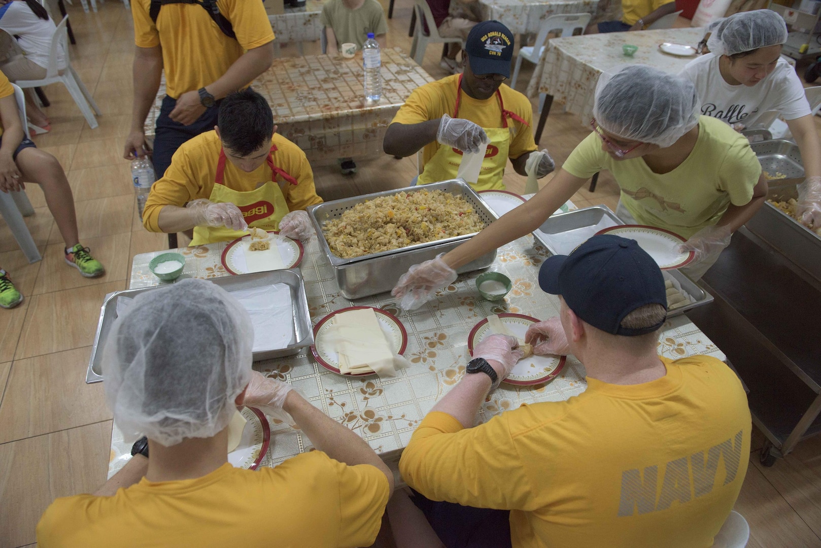Sailors assigned to the aircraft carrier USS Ronald Reagan (CVN 76) prepare spring rolls with Singapore locals during a community relations project at Willing Hearts Soup Kitchen, June 18, 2017. Sailors are scheduled to participate in six community-relations projects, including a food bank, assisting pre-kindergarten and kindergarten teachers, and repairing and painting a church during a scheduled port visit to Singapore. 