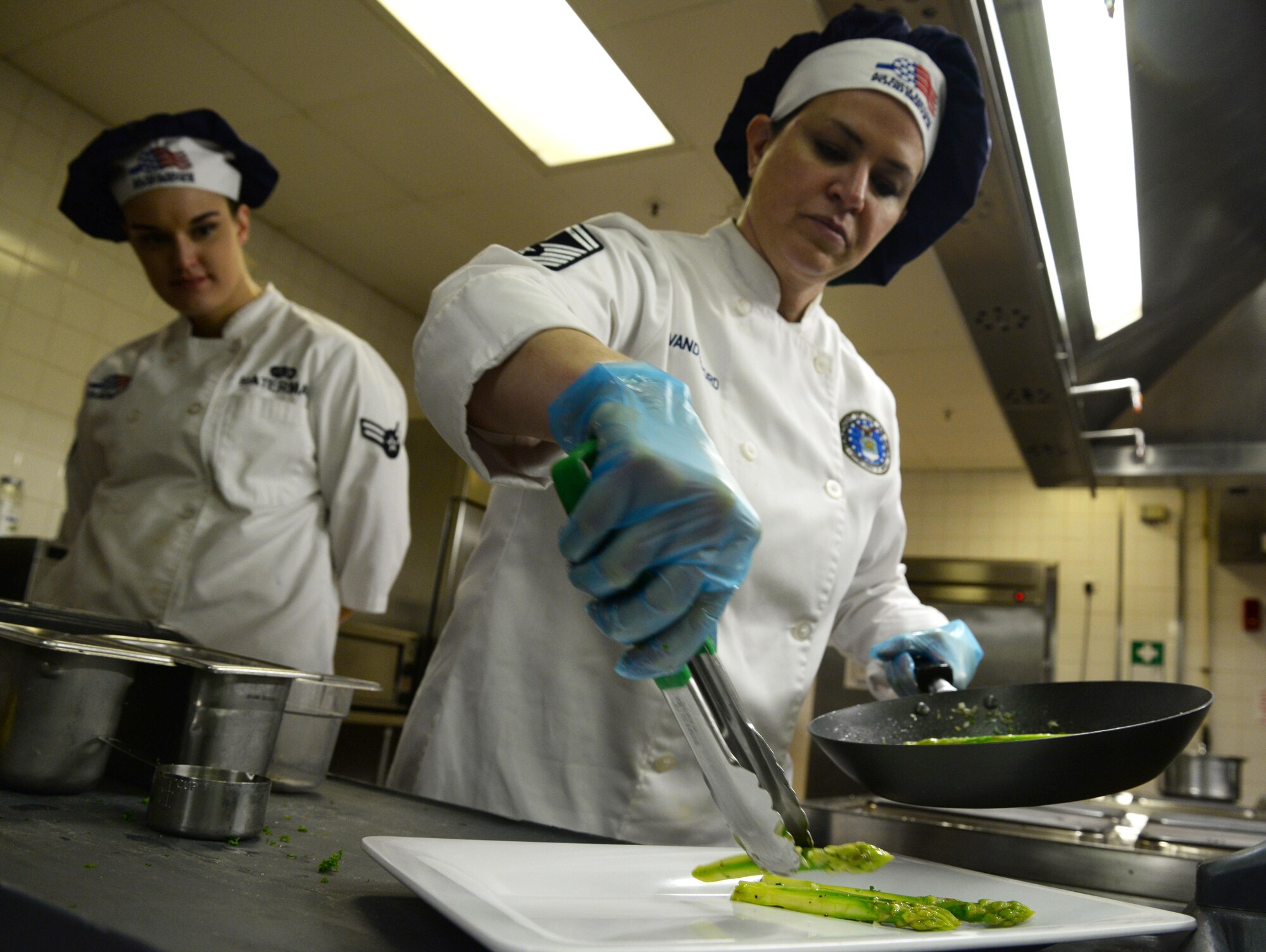 U.S. Air Force Senior Master Sgt. Teresa Vanderford, Air Force General Officer Management Office enlisted aide program manager, right, plates sautéed asparagus at the Gateway Dining Facility on RAF Mildenhall, England, June 8, 2017. The weeklong training took place to reinforce attention to detail and encourage cooks to take pride in their work. (U.S. Air Force photo by Senior Airman Justine Rho)