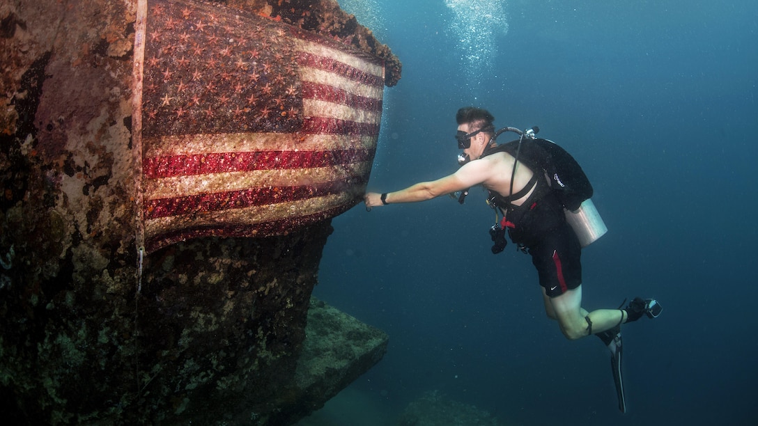 A sailor fixes an American flag on the American Tanker, a sunken concrete barge used to transport fuel during World War II, in Apra Harbor, Guam, June 21, 2017. The sailor is a master chief petty officer assigned to Explosive Ordnance Disposal Group 1. The Navy unit is the world's premier combat force for countering explosive hazards and conducting expeditionary diving and salvage. Navy  photo by Petty Officer 3rd Class Alfred A. Coffield

