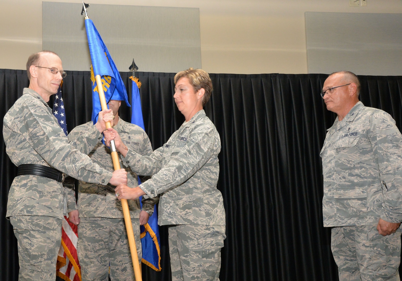 Air Force Maj. Gen. Bart O. Iddins (left), 59th Medical Wing commander at Joint Base San Antonio-Lackand, passes the 59th Training Group guidon to incoming commander Col. Karyn E. McKinney (center) as outgoing commander Col. (Dr.) Steven C. Caberto (right) looks on during the unit’s change of command ceremony at JBSA-Fort Sam Houston June 15. The 59th Training Group develops, delivers and evaluates medical training for 75 medical treatment facilities and deployment operations worldwide. The group supports military medical service and medical readiness training at the Medical Education and Training Campus at JBSA-Fort Sam Houston for 12,100 students annually, as well as two operating locations, one detachment and 17 sites around the world.