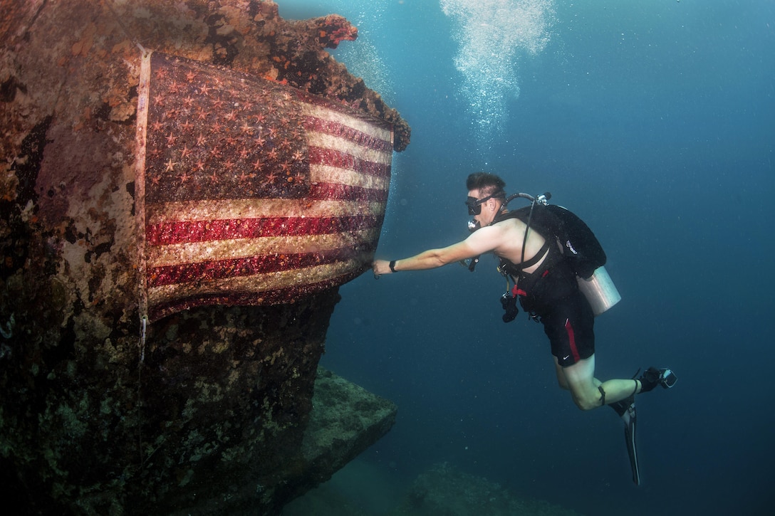 A sailor fixes an American flag on the American Tanker, a sunken concrete barge used to transport fuel during World War II, in Apra Harbor, Guam, June 21, 2017. The sailor is a master chief petty officer assigned to Explosive Ordnance Disposal Group 1. The Navy unit is the world's premier combat force for countering explosive hazards and conducting expeditionary diving and salvage. Navy  photo by Petty Officer 3rd Class Alfred A. Coffield

