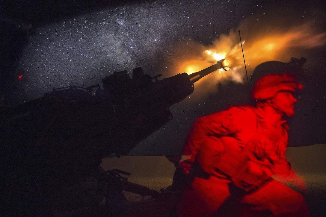 A Marine fires a howitzer in the early morning, creating a yellow flare.
