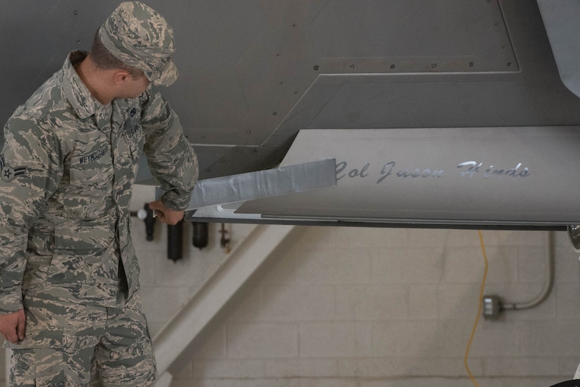 U.S. Air Force Airman 1st Class Jeremy Weymouth, 1st Aircraft Maintenance Squadron assistant dedicated crew chief, reveals U.S. Air Force Col. Jason Hinds, 1st Fighter Wing commander’s name on the flag ship F-22 Raptor, Joint Base Langley-Eustis, June 23, 2017. Hinds assumed command of the 1st FW from U.S. Air Force Col. Peter Fesler during the change of command ceremony. (U.S. Air Force photo by Staff Sgt. Carlin Leslie)