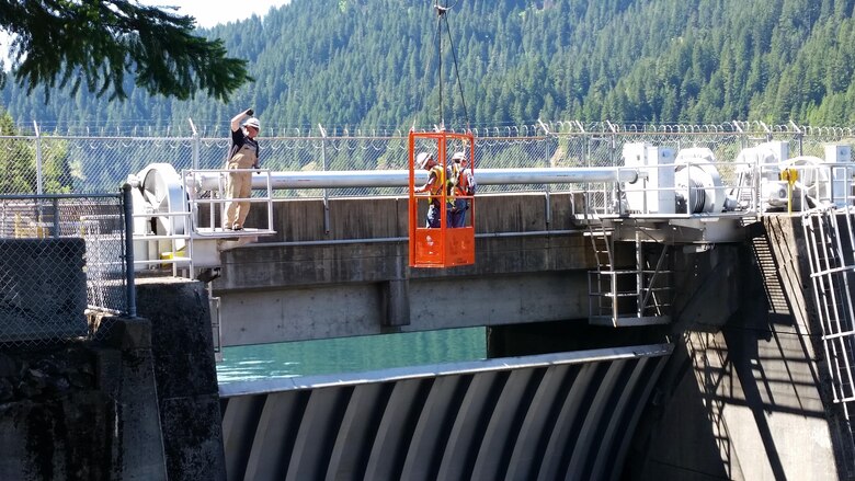 A pair of inspectors dangle high above the spillway of Cougar Dam in a crane bucket, while another Portland District teammate directs the crane operator, May 24. This team of geotechnical, geological, hydraulic, structural and mechanical engineers examined the dam during the periodic inspection, which happens every five years.