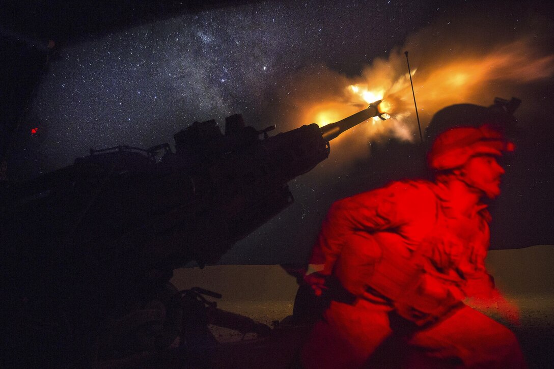 A Marine fires a howitzer in the early morning, creating a yellow flare.