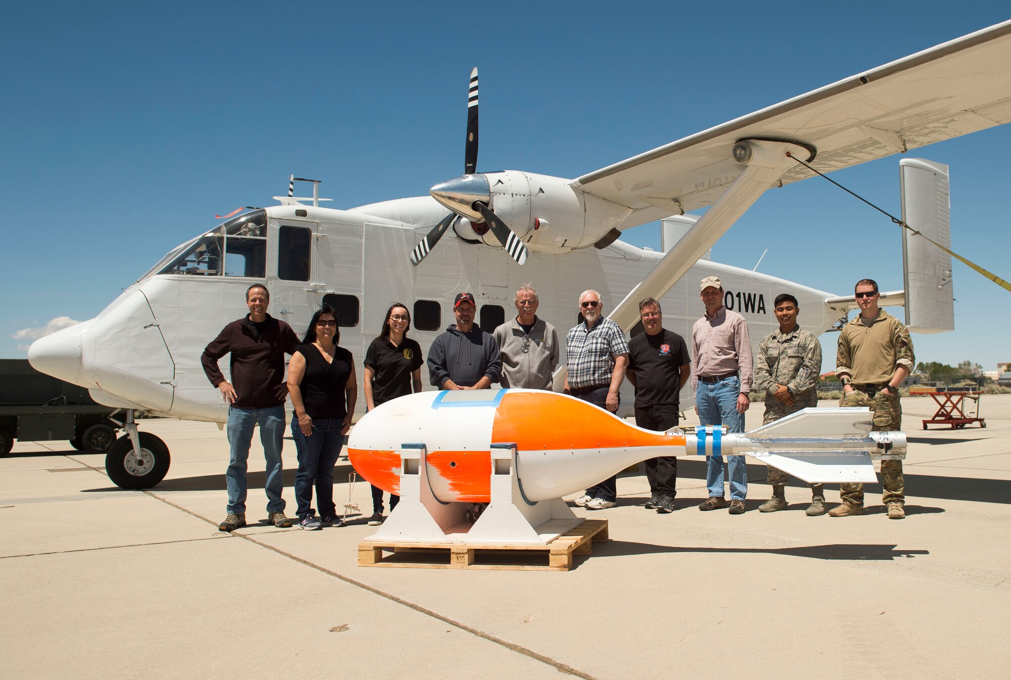 Some of the members of the 418th Flight Test Squadron pose in front of the Skydive Perris Skyvan aircraft used in testing of the GR7000 parachute along with a crosswind deployment cylindrical test vehicle (foreground) that was also used. (U.S. Air Force photo by Ethan Wagner)