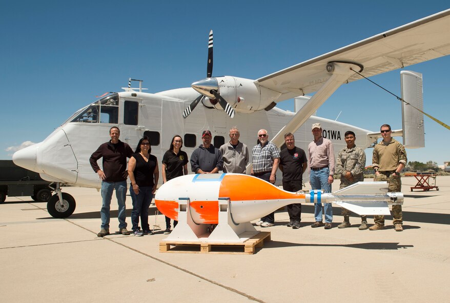 Some of the members of the 418th Flight Test Squadron pose in front of the Skydive Perris Skyvan aircraft used in testing of the GR7000 parachute along with a crosswind deployment cylindrical test vehicle (foreground) that was also used. (U.S. Air Force photo/Ethan Wagner)