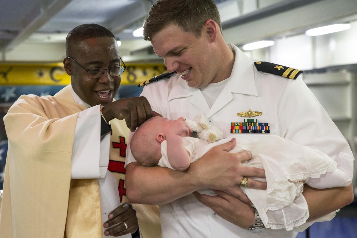 A sailor holds his son during a baptism ceremony on a ship.
