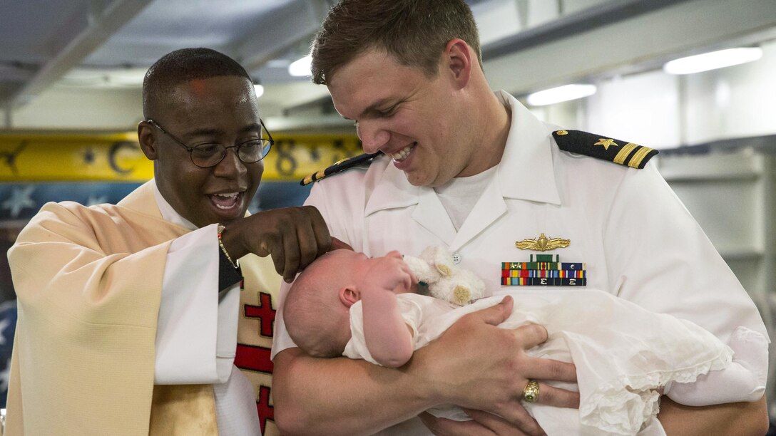 Navy Lt. John "Jack" Curren holds his son during a baptism ceremony on the Pre-Commissioning Unit Gerald R. Ford in Norfolk, Va., June 24, 2017. This was the Ford's first onboard baptism. Navy photo by Petty Officer 3rd Class Cathrine Mae O. Campbell
