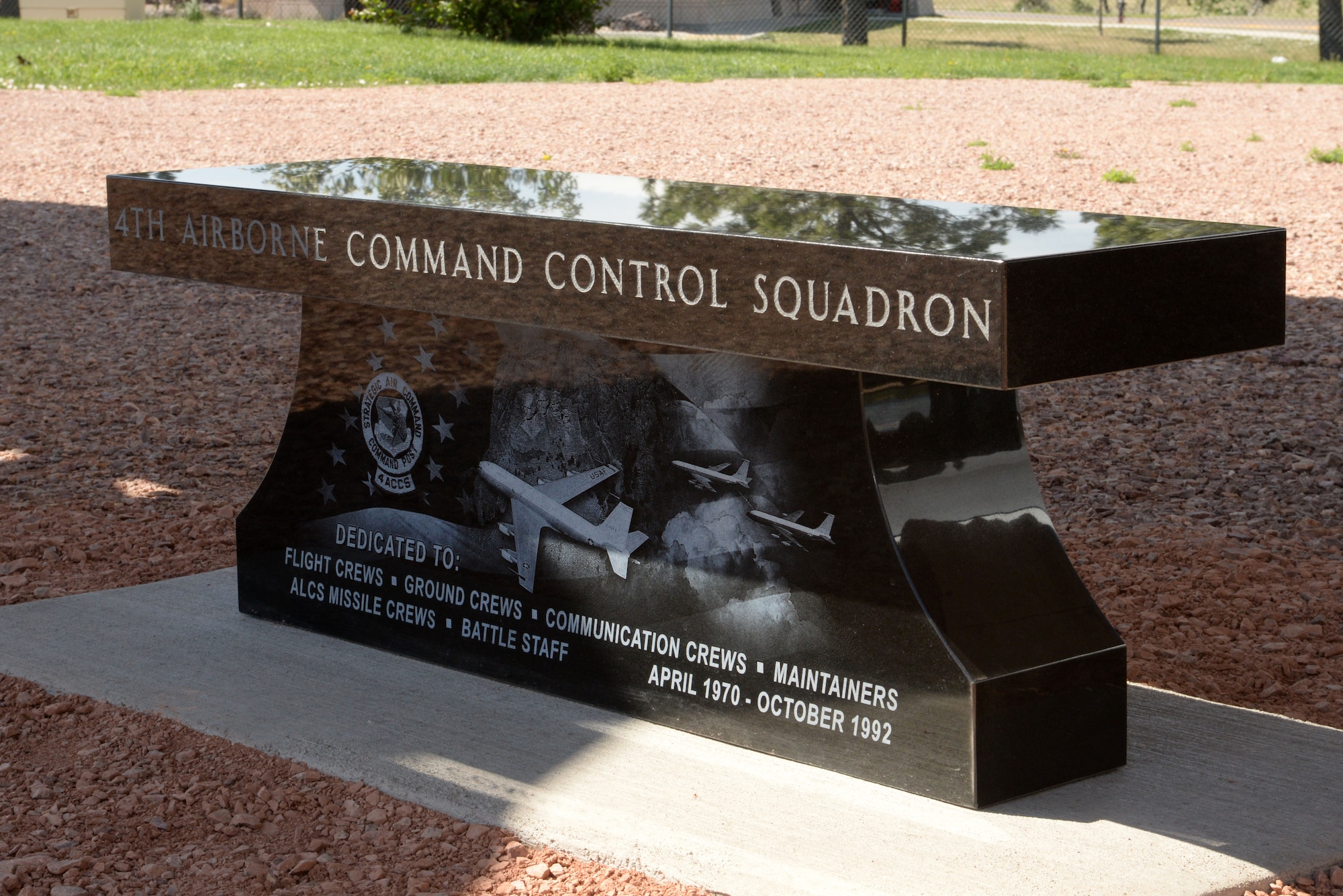 The 4th Airborne Command Control Squadron memorial bench sits on the grounds at the South Dakota Air and Space Museum, Box Elder, S.D., June 24, 2017. The memorial includes an American flag flying in the background with an image of an EC-135 aircraft flying over Mount Rushmore at the center; an image of two EC-135s conducting in-flight refueling to the right; and the squadron patch on the left. (U.S. Air Force photo by Staff Sgt. Hailey Staker)