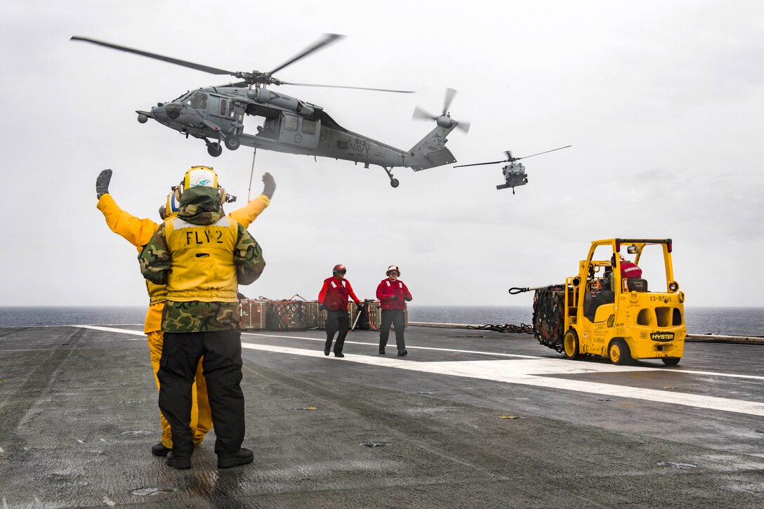 Sailors direct a Navy MH-60S Sea Hawk helicopter to lift ammunition crates from the flight deck of the aircraft carrier USS Dwight D. Eisenhower during an ammunition offload with the dry cargo and ammunition ship USNS Medgar Evers in the Atlantic Ocean, June 21, 2017. Navy photo by Seaman Jessica L. Dowell