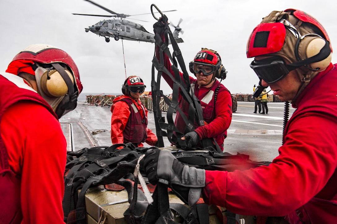 Navy Petty Officer 2nd Class Aaron Jenkins, center, secures a cargo net around an ammunition crate on the flight deck aboard the aircraft carrier USS Dwight D. Eisenhower during an ammunition offload with the dry cargo and ammunition ship USNS Medgar Evers in the Atlantic Ocean, June 21, 2017. Jenkins is an aviation ordnanceman. Navy photo by Seaman Jessica L. Dowell