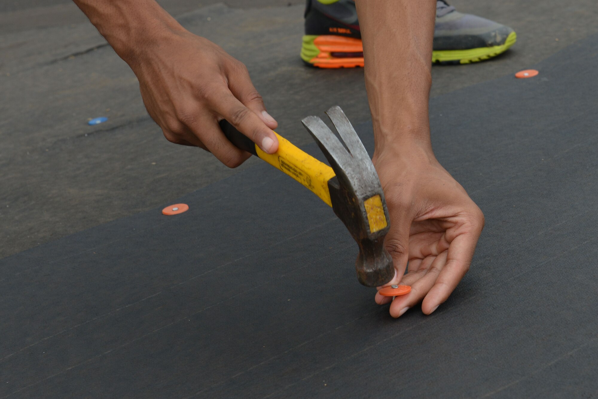 U.S. Air Force 2nd Lt. Michael McDowell, 20th Contracting Squadron contract specialist, hammers a nail to keep weather-proofing tarp material in place in Sumter, S.C., June 23, 2017. McDowell placed the tarp to water-proof the roof, helping to protect the top of the house from rain. (U.S. Air Force photo by Airman 1st Class Destinee Sweeney)