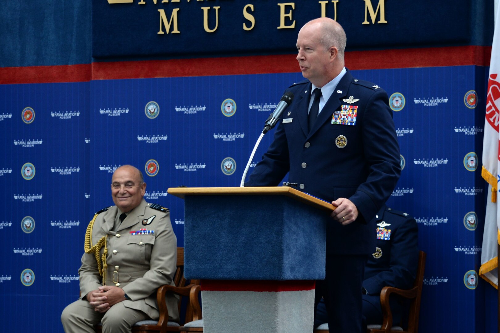 Col. Joel Carey, 12th Flying Training Wing commander provides closing comments as guest speaker while Air Chief Marshal Stuart Peach, Chief of the Defence Staff of the United Kingdom looks on during the Combat Systems Officer graduation, inside the National Naval Aviation Museum at Naval Air Station Pensacola, Florida, June 23, 2017. 