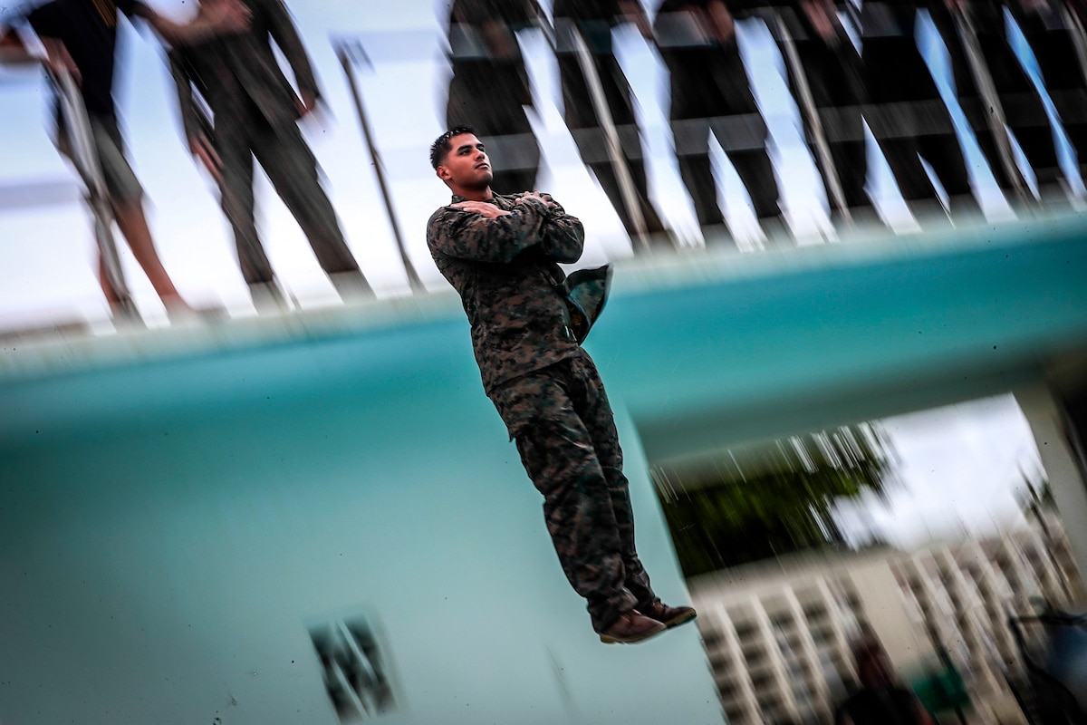 A Marine folds him arms as he jumps from a tower into a pool.