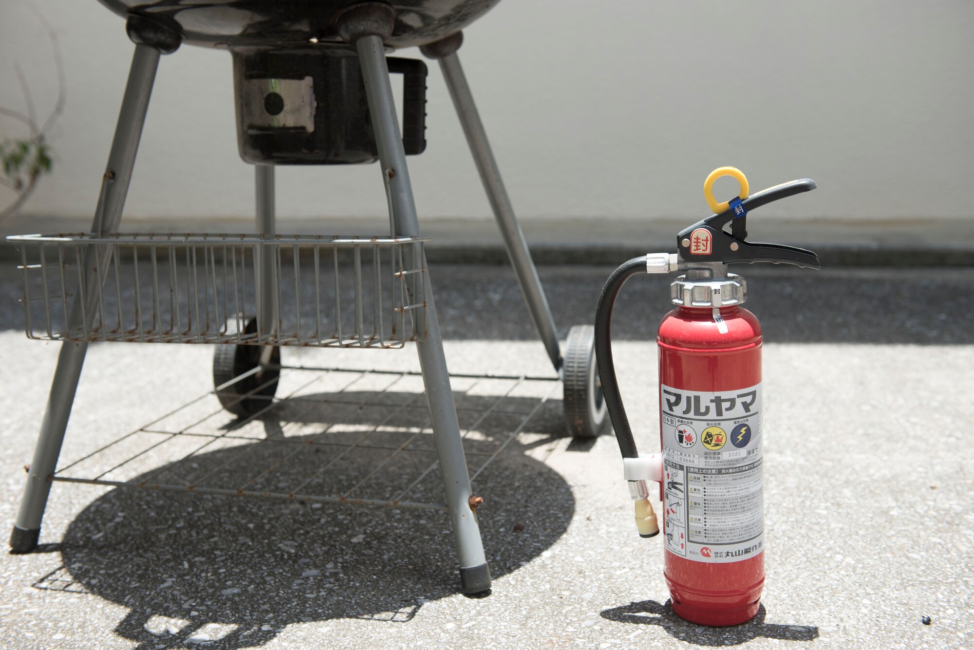 A fire extinguisher sits next to a grill June 28, 2017, at Kadena Air Base, Japan. Maintaining a fire extinguisher is especially important to help control a fire in the event of an emergency. (U.S Air Force photo by Senior Airman Quay Drawdy)