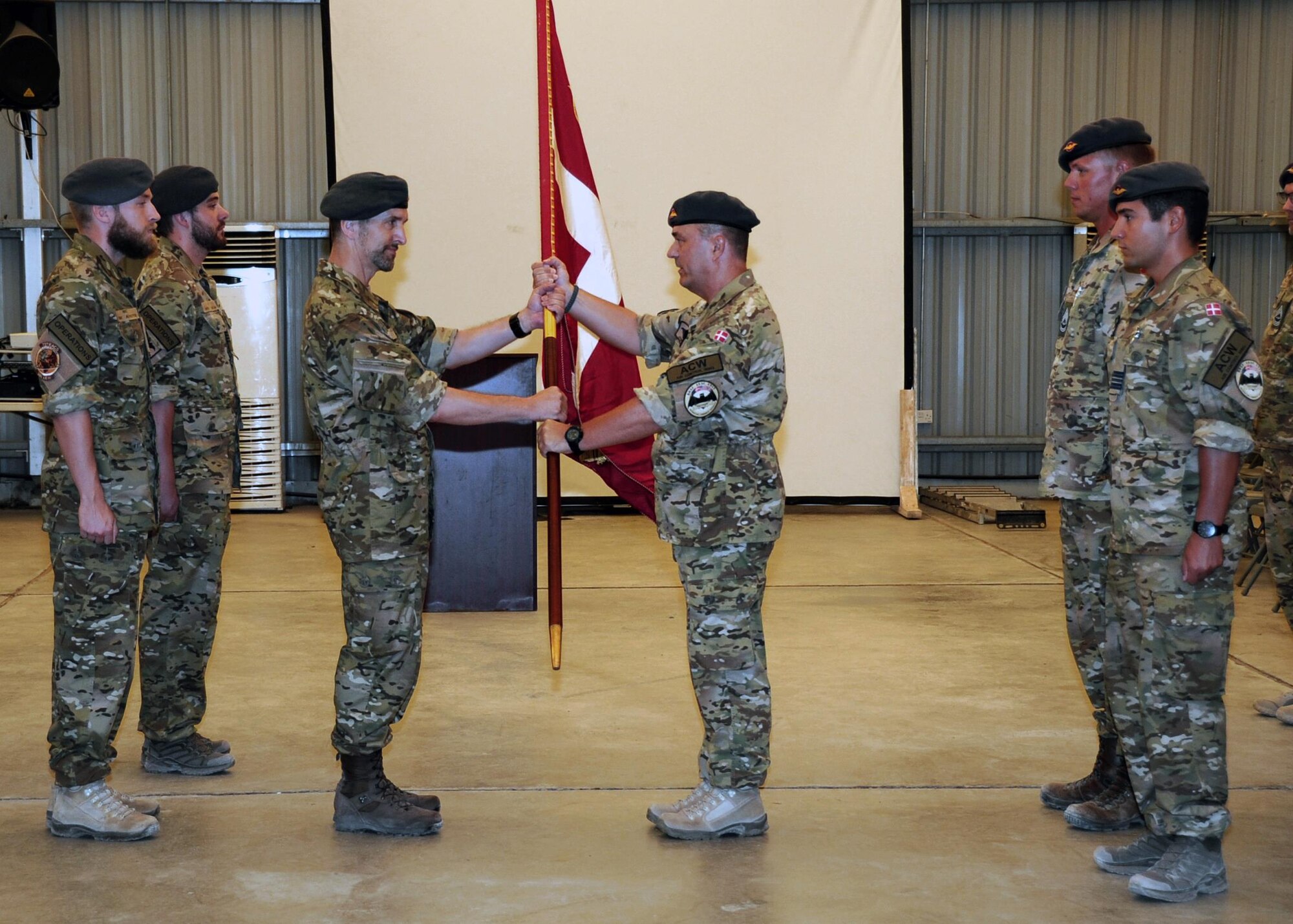 Royal Danish Air Force Lt. Col. John Pedersen, right, Team 7 Detachment commander, passes the Dannebrog, national flag of Denmark, to Royal Danish Air Force Lt. Col. Claus Pedersen, left, Team 8 Detachment commander, during a change of command ceremony June 29, 2017, at an undisclosed location in southwest Asia. As Coalition partners of the 380th Air Expeditionary Wing, both Team 7 and Team 8 members serve as integrated colleagues of the 727th Expeditionary Air Control Squadron. (U.S. Air Force Photo by Senior Airman Preston Webb)