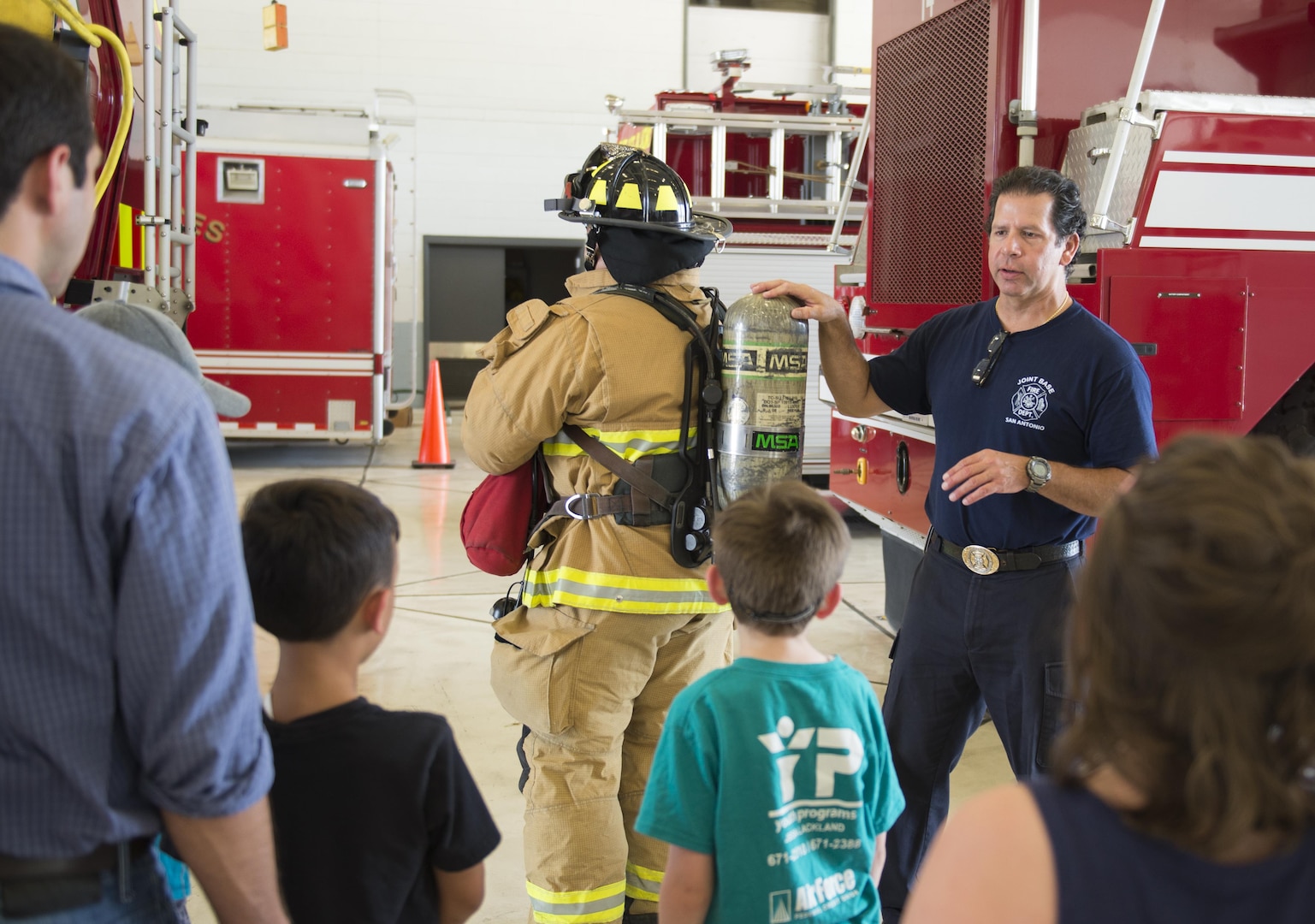 Jeffery Pardo (left), 502nd Civil Engineering Squadron firefighter, wears his fire protection gear as Michael Martinez, 502nd CES firefighter, talks about the different equipment to children from Vibrant ABA Solutions during a open house tour of Fire Station 2 June 23, 2017, at Joint Base San Antonio-Lackland, Texas. One of the goals of hosting tour is to make children more comfortable with firefighters wearing their full gear so they won’t be frightened during an emergency. (U.S. Air Force photo by Senior Airman Krystal Wright)