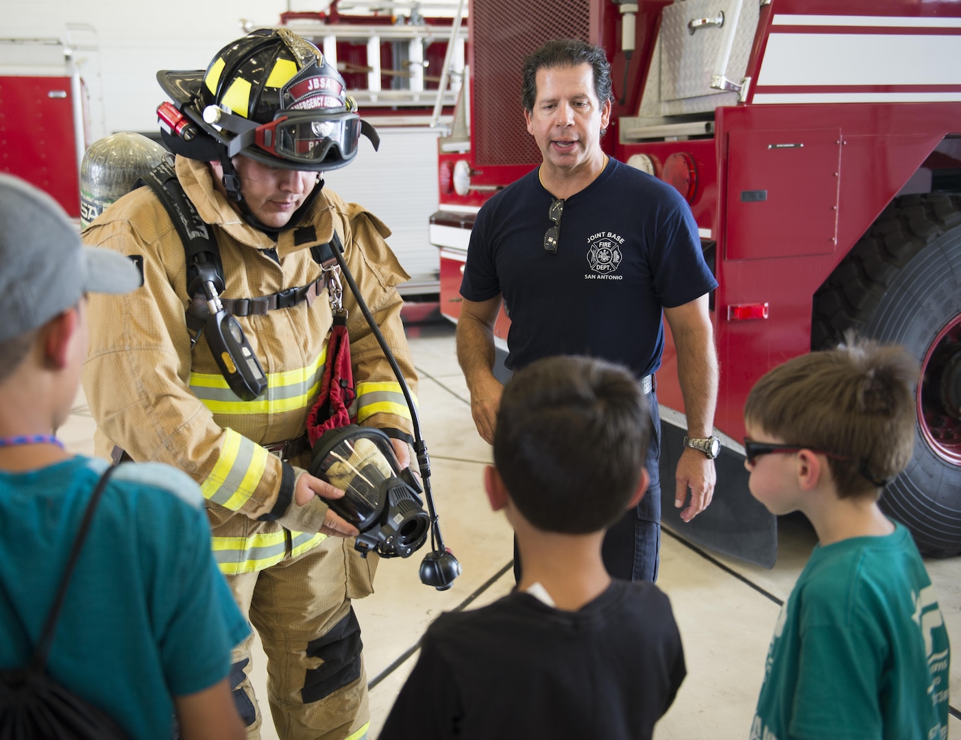 Jeffery Pardo (left), 502nd Civil Engineering Squadron firefighter, shows off his fire protection gear as Michael Martinez, 502nd CES firefighter, explains it to children from Vibrant ABA Solutions during a open house tour of Fire Station 2 June 23, 2017, at Joint Base San Antonio-Lackland, Texas. (U.S. Air Force photo by Senior Airman Krystal Wright)