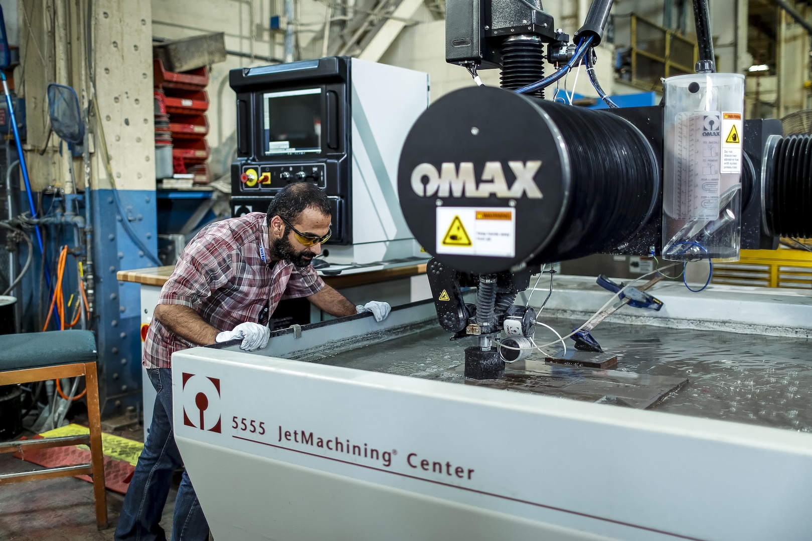 A Norfolk Naval Shipyard worker monitors a precision water cut on the shipyard's new water jet cutting machine. The shipyard uses the water jet cutting machine to fabricate new parts or replace worn parts during maintenance availabilities. The machine cuts a wide variety of materials using a high- pressure jet of water mixed with an abrasive substance. It was purchased and installed as part of NAVSEA's efforts to replace worn equipment and improve productivity.