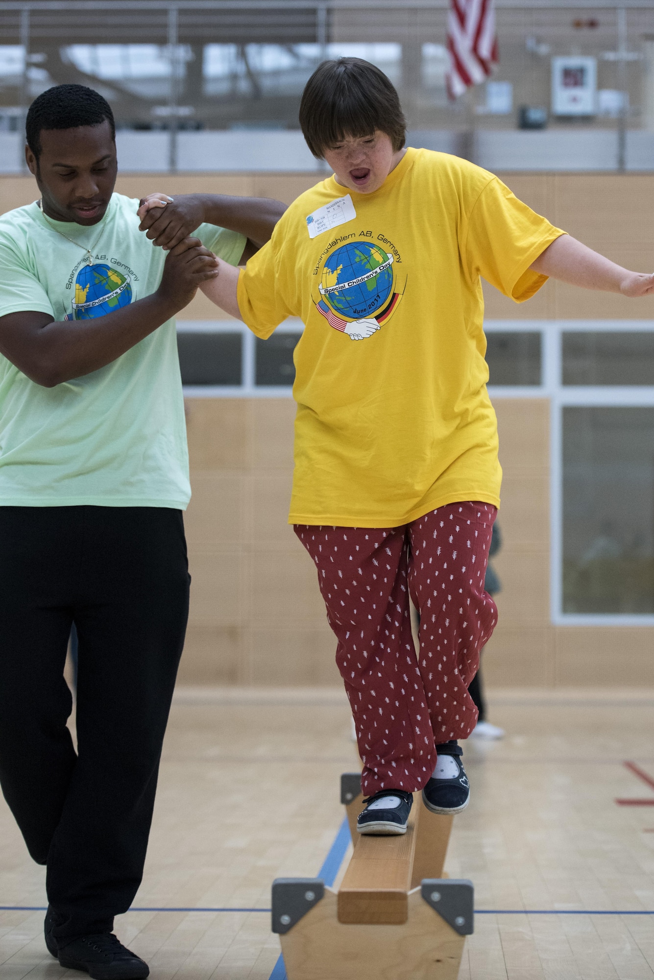 U.S. Air Force Senior Airman Javier Boswell, 52nd Logistics Readiness Squadron supply technician, helps Nina Mandernach, student from Bitburg, walk across an obstacle during the St. Martin Special Children's Day at Spangdahlem Air Base, Germany, June 28, 2017. Each student from the event was paired up with a volunteer to participate in a variety of activities to include basketball throw, hula-hooping, balance beam and bowling. (U.S. Air Force photo by  Senior Airman Preston Cherry)