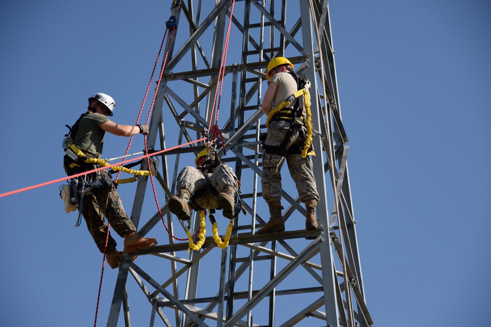 Airman 1st Class Ryan Ferguson, 364th Training Squadron cables and antenna systems apprentice course student, trains on how to do a ground based belay assist tower rescue, while his instructor, Cpl. Alex Shepley, and classmate, Airman MeKail Merritt, look on.  Several situations like equipment failure or injury could leave the climber unable to descend the tower on their own. This method is the safest method of retrieving someone from the tower because it only puts the person descending at risk, no one else.