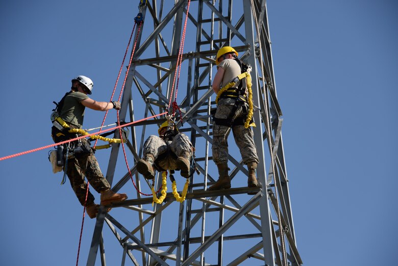 Airman 1st Class Ryan Ferguson, 364th Training Squadron cables and antenna systems apprentice course student, trains on how to do a ground based belay assist tower rescue, while his instructor, Cpl. Alex Shepley, and classmate, Airman MeKail Merritt, look on.  Several situations like equipment failure or injury could leave the climber unable to descend the tower on their own. This method is the safest method of retrieving someone from the tower because it only puts the person descending at risk, no one else.