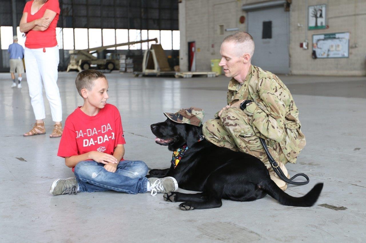 Army Chief Warrant Officer 4 Chris Hellums and his son, Gabriel, sit with Kyle, an ambassador dog for Southeastern Guide Dogs, at Hunter Army Airfield, Ga., June 26, 2017. Kyle became the ambassador dog after being diagnosed with an injury. Army photo by Staff Sgt. Kellen Stuart