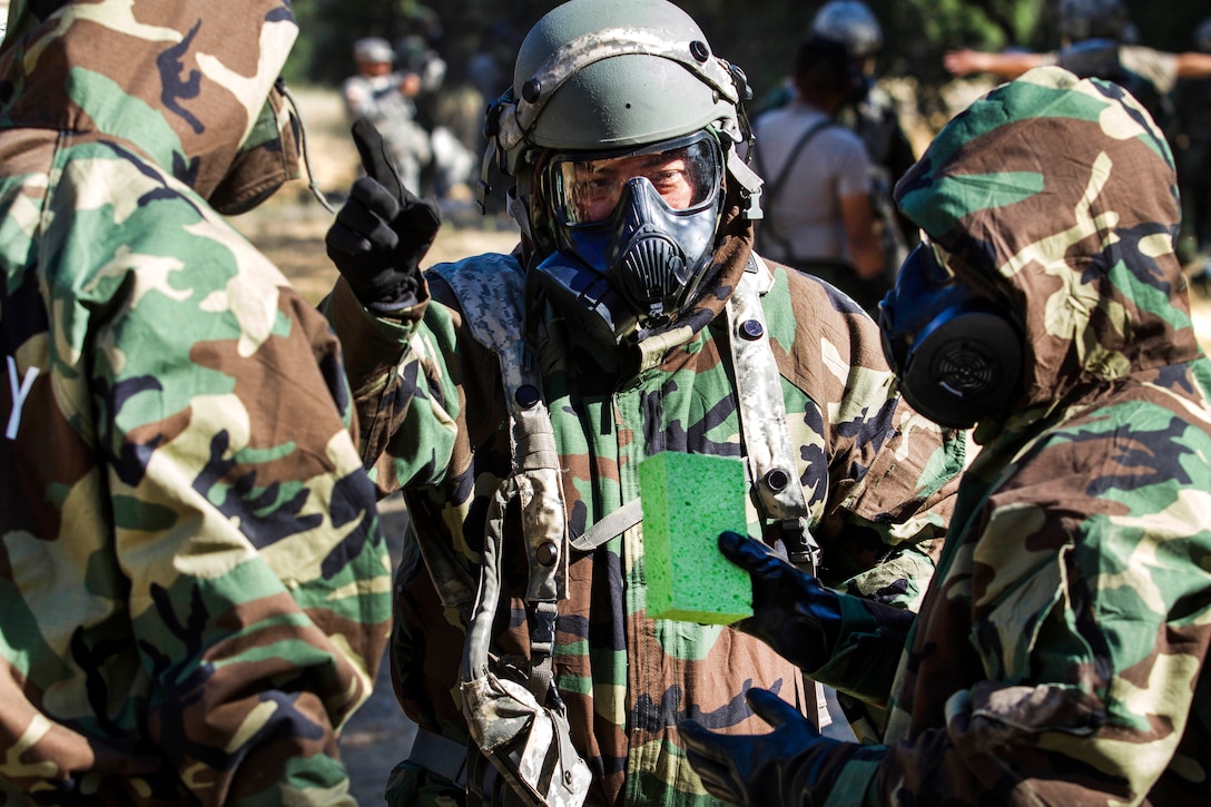 Army Spc. Juan Ibarral, center, instructs soldiers on washing their gas masks during a decontamination mission, part of Warrior Exercise at Fort Hunter Liggett, Calif., June 21, 2017. Ibarral is assigned to the Army Reserve's 340th Chemical Company. Army photo by Spc. Derek Cummings 
