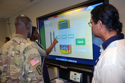 Medical Education and Training Campus medical illustrator Shevon Barnes and METC visual information specialist Louis Fernandez speak with Lt. Col. Amy Roberson, program director for the METC surgical technician course, about the 3D interactive skeletal model demonstration on a SMART interactive display board. 