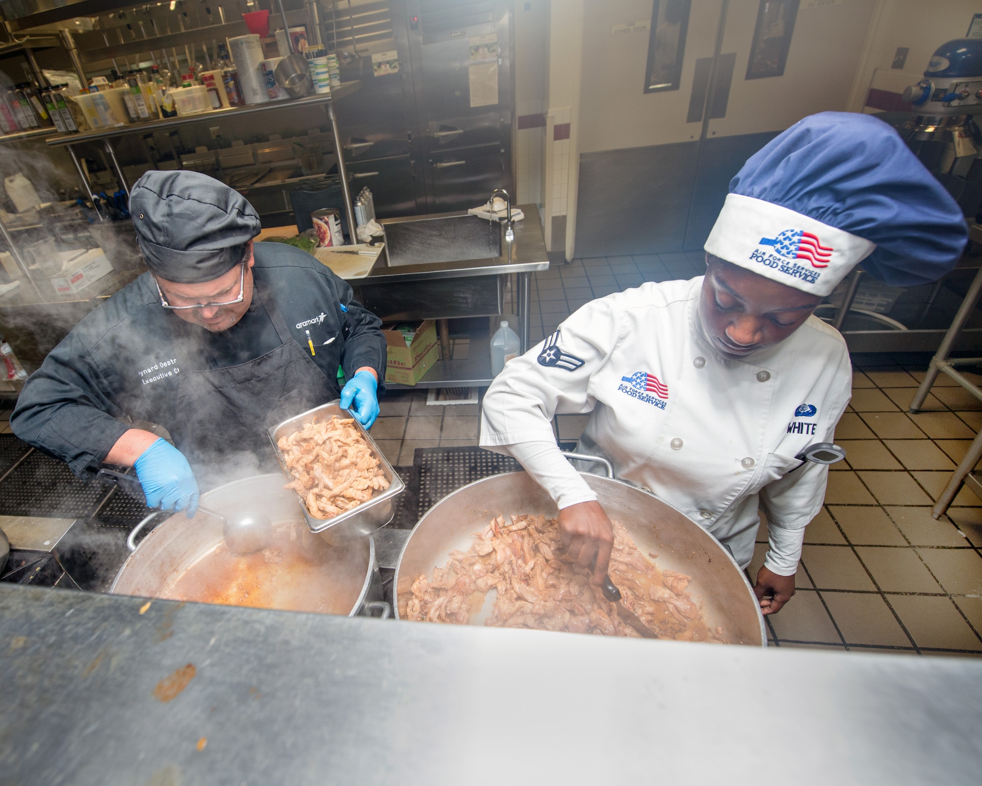 Maynard Oestreich, executive chef for Aramark and U.S. Air Force Airman 1st Class Cierra White with the 60th Force Support Squadron, prepare meals prior to the BIBIM Box tasting featuring Korean food at Sierra Inn Dining Facility, Travis Air Force Base, Calif., June 29, 2017. Oestreich a former U.S. Navy veteran and an award-winning chef from Napa Valley, Calif., took the head chef position so he could mentor young Airmen. (U.S. Air Force photo by Louis Briscese)