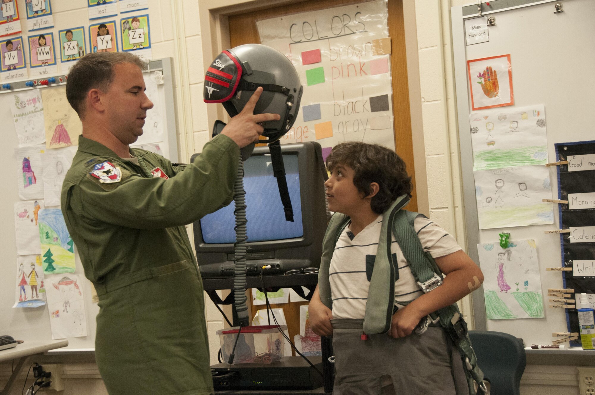 Col. Tom Bladen, 104th Fighter Wing operations group commander, visits refugee students at Highland Elementary School in Westfield, Massachusetts, June 26, 2017. The visit served as a means to help the children understand why they hear the loud screeching F15 jets flying overhead when playing outside and to help them understand the 104th Fighter Wing flies to protect. Bladen helps the honoree pilot of the day dawn a 104th Fighter Wing flight suit. (U.S. Air National Guard photo by Senior Master Sgt. Julie Avey)