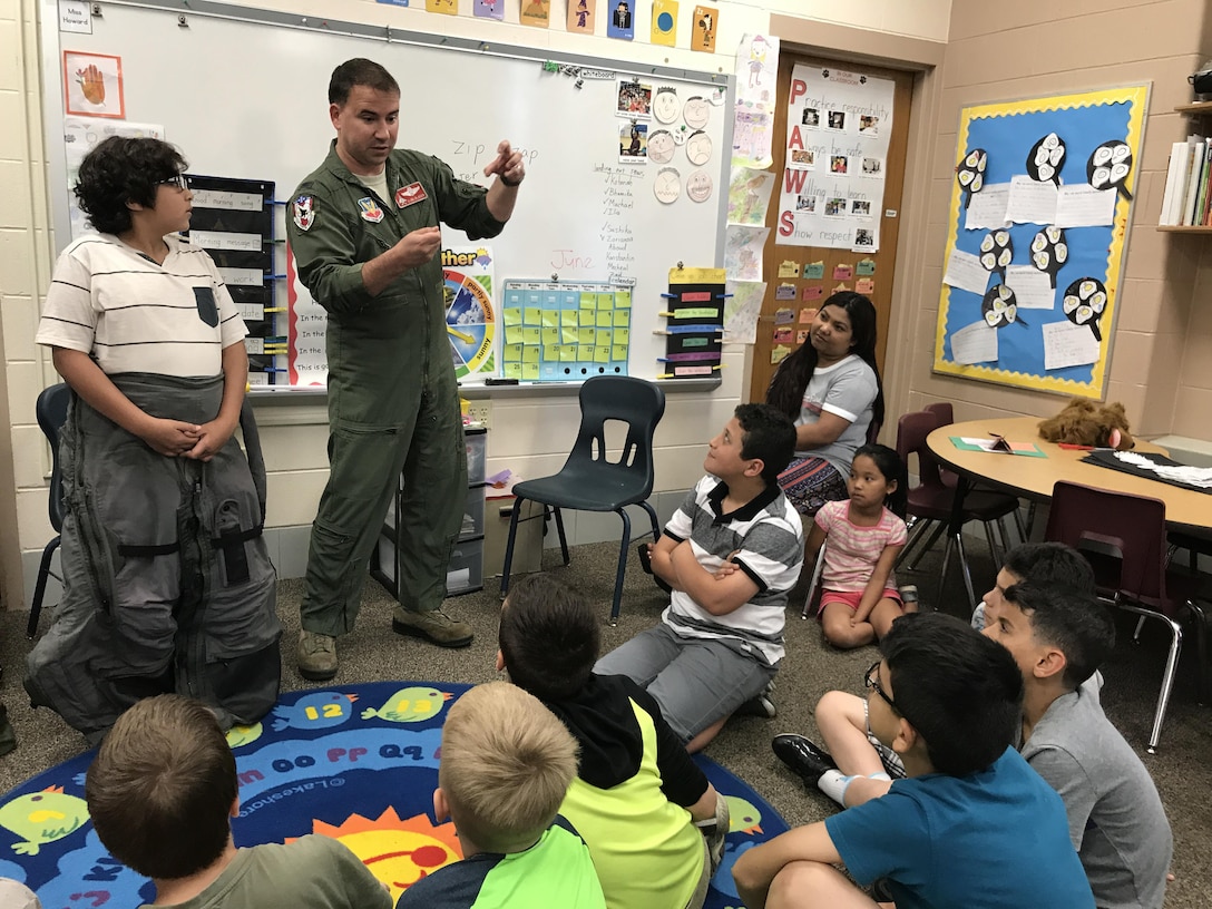 Col. Tom Bladen, 104th Fighter Wing operations group commander, visits refugee students at Highland Elementary School in Westfield, Massachusetts, June 26, 2017. The visit served as a means to help the children understand why they hear the loud screeching F15 jets flying overhead when playing outside and to help them understand the 104th Fighter Wing flies to protect. Bladen explains how the flight suit prevents the pilots from passing out while flying as he speaks to the students after helping the honoree pilot of the day dawn a 104th Fighter Wing flight suit. (U.S. Air National Guard photo by Senior Master Sgt. Julie Avey)