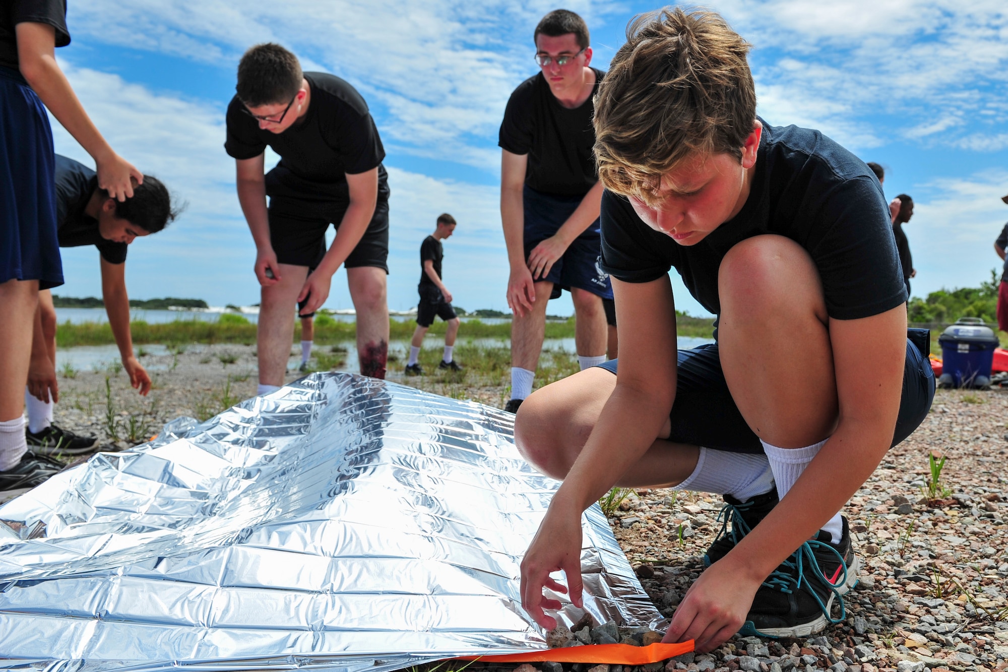A Junior ROTC cadet anchors down a reflective blanket to make a rescue signal during survival, evasion, resistance and escape training at Hurlburt Field, Fla., June 29, 2017. SERE specialists with the 1st Special Operations Support Squadron gave Summer Leadership School cadets a crash course on SERE, including signaling aircraft, starting fires with natural resources, and crafting shelters in the wilderness. (U.S. Air Force photo by Staff Sgt. Victor J. Caputo)