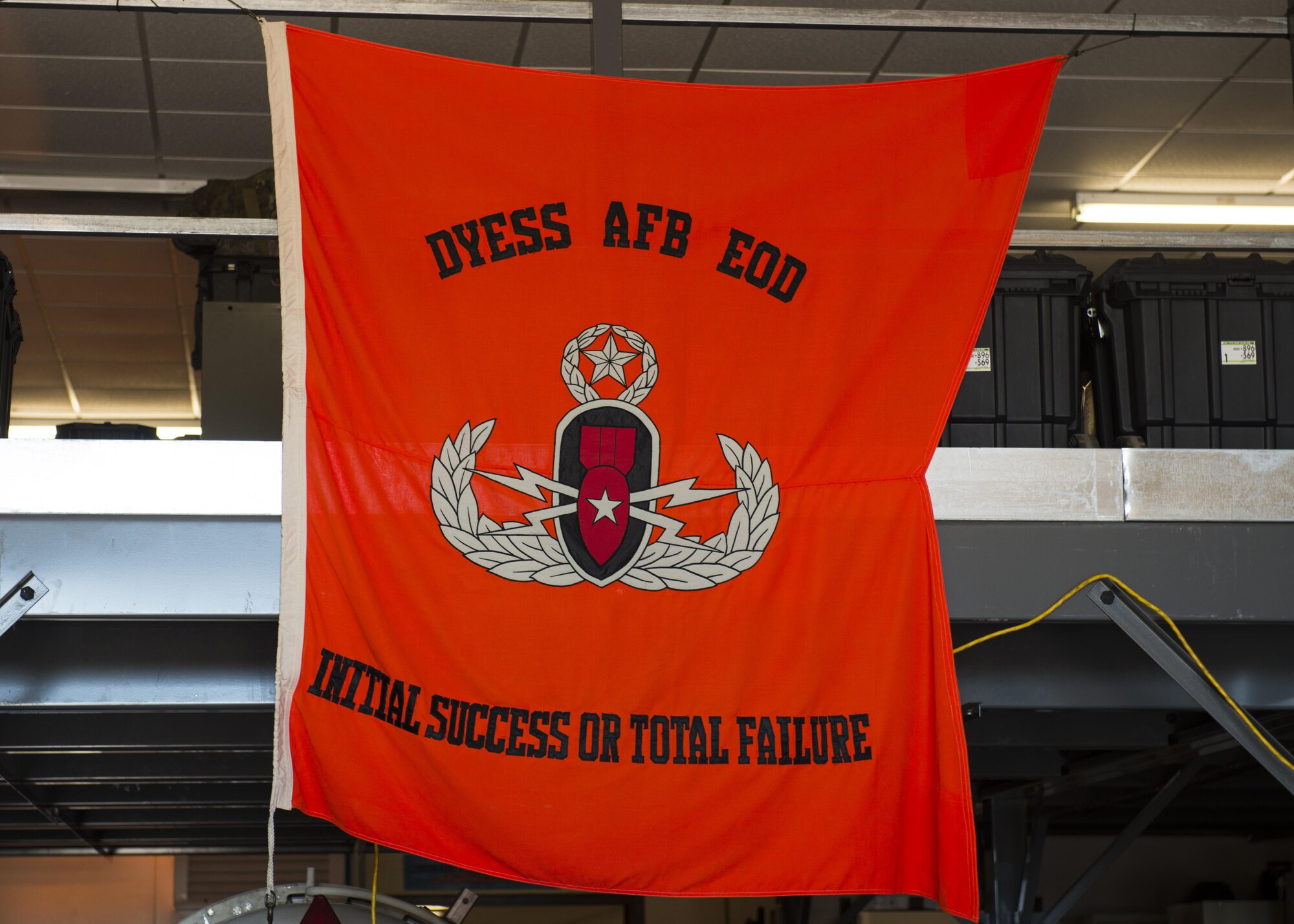 A flag reading the explosive ordnance disposal motto, “Initial success or total failure”, hangs from the ceiling of the 7th Civil Engineer Squadron EOD flight building at Dyess Air Force Base, Texas, June 28, 2017. EOD Airmen are tasked to identify, locate and if necessary, defuse any explosives that may pose a threat to the base and its assets. (U.S. Air Force photo by Senior Airman Katherine Miller)