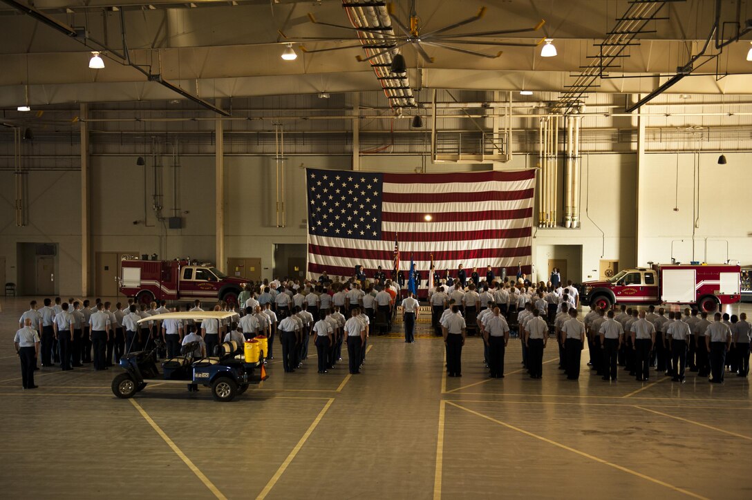 The 316th Training Squadron and visitors stand for the singing of the National Anthem during the 316th TRS Change of Command ceremony at the Fire Academy high bay on Goodfellow Air Force Base, Texas, June 30, 2017. The ceremony bade farewell to  the previous commander, Lt. Col. Wendie Mount and welcomed the new commander, Lt. Col. Robert Kammerer. (U.S. Air Force photo by Senior Airman Scott Jackson/Released)