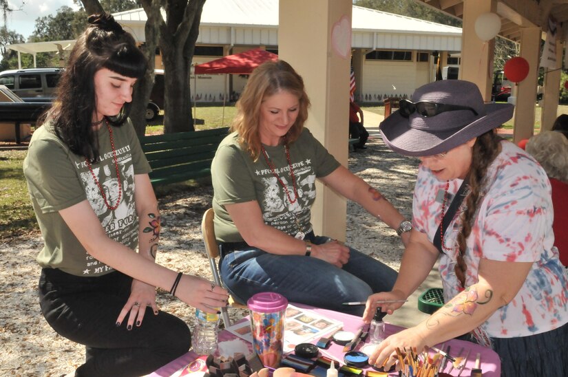 Alexis Kirk (left) and mother Annette Kirk (middle) get flowers painted on their arms by USO volunteer Brenda Ross (right) during Operation Love Letters.  Annette lost a son, Pfc. Paul Cuzzupe, during combat operations in Afghanistan in 2010.  This activity is part of Operation Love Letters, which  is an annual patriotic celebration to honor fallen service members through fellowship with family and friends gathered together writing love letters, scripting poetry, sharing loveable memories of their service member, and enjoying the offerings of some very special guests. This year, the event was held at Veterans Memorial Park in Tampa on Feb. 19, 2017.