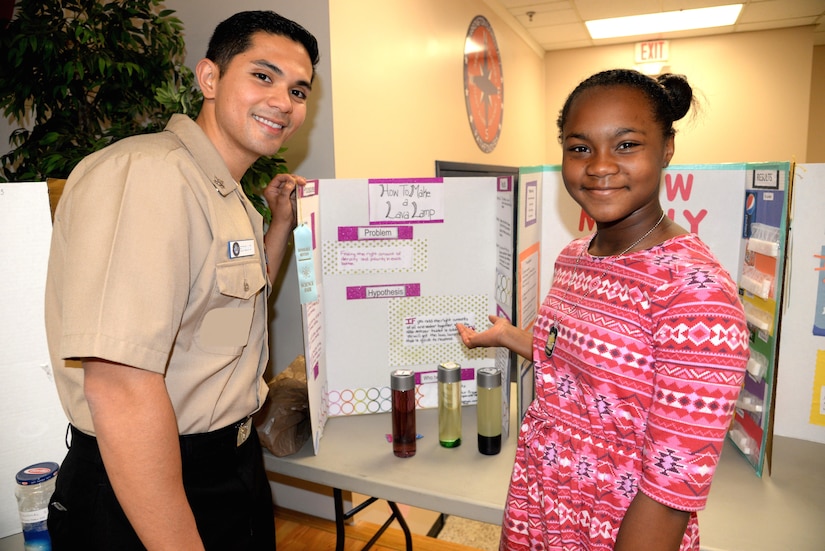 Kaitlynn Funches, 10, a fourth-grade student (right) at Marrington Elementary (MNE) School, located at Joint Base Charleston – Weapons Station, explains her science fair project to Navy Petty Officer 2nd Class Francis Edquid, left, a radiologic technologist serving at Naval Health Clinic Charleston. Edquid was one of the judges during the Marington Elementary School Science Fair Feb. 21. Funches earned an Honorable Mention for her project, "How to Make a Lava Lamp."