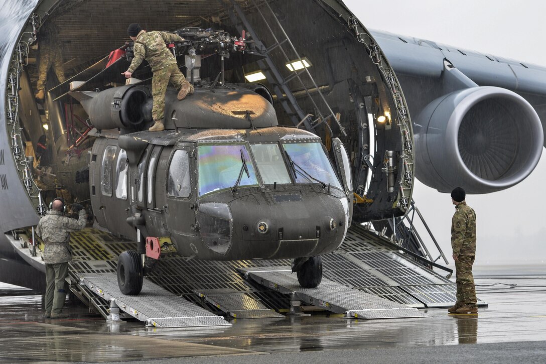 A soldier slowly directs a UH-60 Black Hawk helicopter down the ramp of an Air Force C-5 Galaxy aircraft at Riga International Airport, Latvia, March 1, 2017. The soldier is assigned to the  10th Combat Aviation Brigade Task Force Phoenix, led by 3rd General Support Aviation Battalion, 10th Aviation Regiment. The rapid assembly demonstrates the unit's ability to lead and provide aviation support to regional and global military forces at a moment's notice to support NATO interests. Army photo by Spc. Shiloh Capers