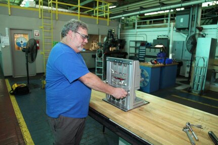 Electrical mechanic Nolan Lloyd secures a molded case circuit breaker to a newly-designed test stand. The new test stand design improves worker safety and reduces the number of workers needed to conduct testing.