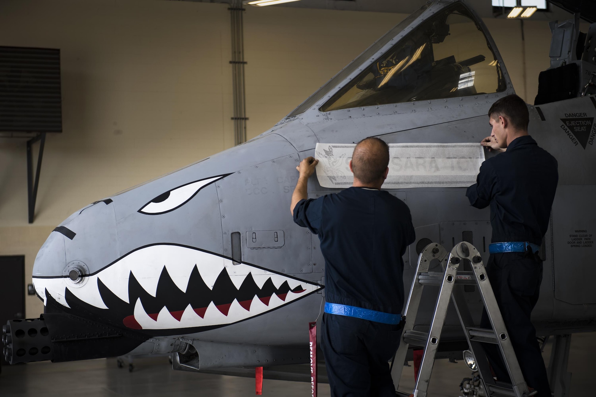 Senior Airmen Kyle Baker and Michael Verheyden, 74th Aircraft Maintenance Unit dedicated crew chiefs, apply a nametape to assign the A-10C Thunderbolt II in the Weapons Load Training hangar to the late Staff Sgt. Sara Toy, 74th AMU weapons team chief, Feb. 27, 2017, at Moody Air Force Base, Ga. Team Moody’s weapons community wanted to honor Toy, who died in a motor vehicle accident on Feb. 25, 2017, by dedicating the aircraft used for training and certifying all weapons load crew members. (U.S. Air Force photo by Andrea Jenkins/Released)