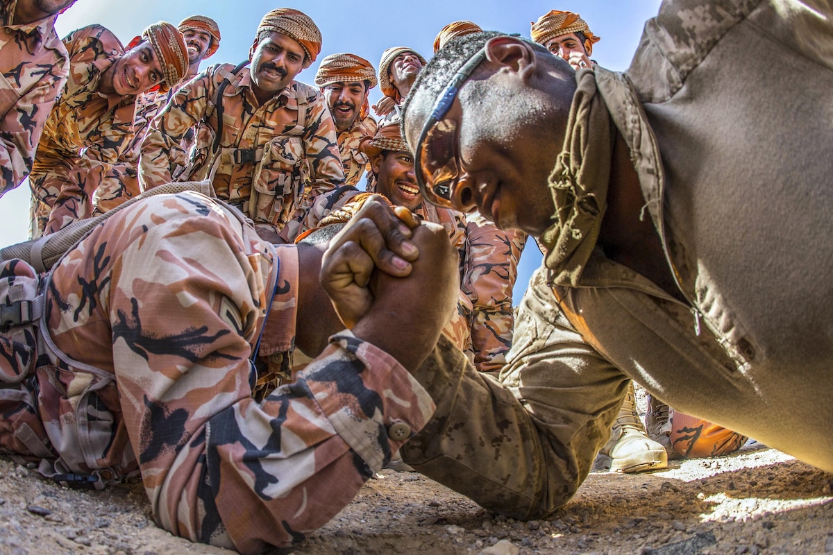 A Marine arm wrestles an Omani soldier on the ground.