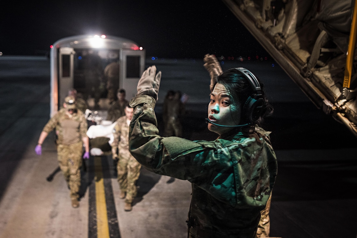 An airman directs troops bringing a patient onto a C-130J Hercules for transport.