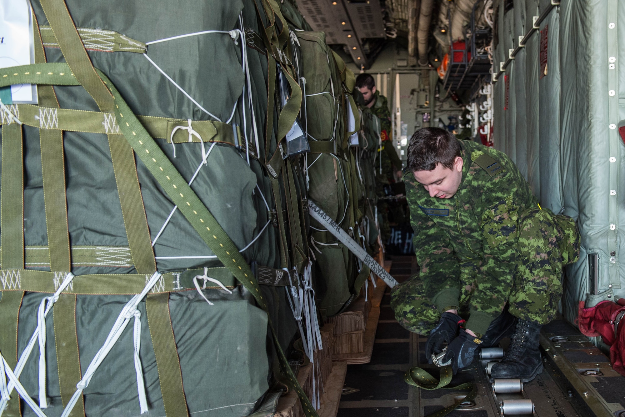 Pvt. Phil Bilodeav, a Royal Canadian Air Force traffic technician, straps down cargo onto a C-130J Super Hercules aircraft before take-off Feb. 10, 2016, at Alexandria International Airport, LA. During the exercise, the two countries integrated their aerial port operations to get a better understanding on how each country operate while loading aircraft. (U.S. Air Force photo by Staff Sgt. Robert Hicks)