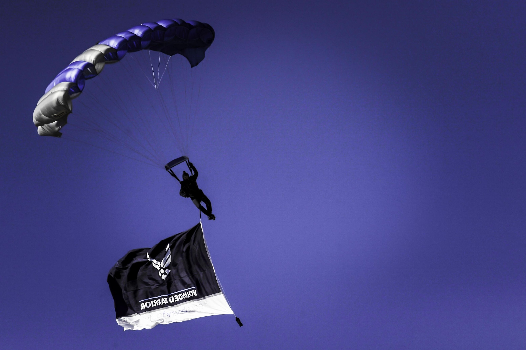 An Air Force Wings of Blue member descends to the ground with the wounded warrior flag during the 2017 Air Force Wounded Warrior Trials opening ceremony on Nellis Air Force Base, Nev., Feb. 24, 2017. The Trials are an adaptive sports event designed to promote the mental and physical well-being of seriously ill and injured military members and veterans. (U.S. Air Force photo by Airman 1st Class Kevin Tanenbaum/Released)