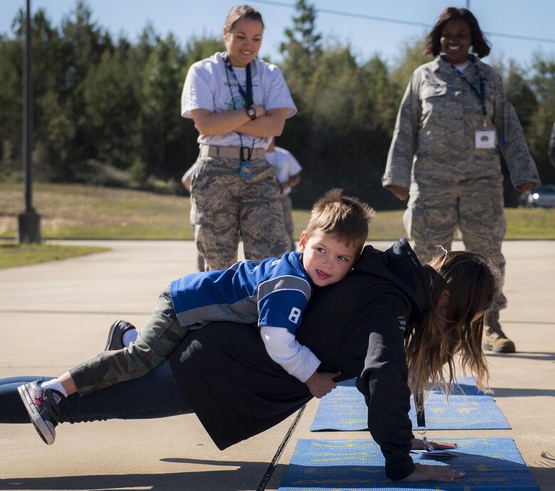 A Wingman “helps” a new 919th Special Operations Wing deployer complete her push-ups during the Operation Hero event at Duke Field, Fla., March 4.  The wing held a mock deployment for the Reserve children to include a deployment line, simulated flight and a “down range” location with games and displays.  (U.S. Air Force photo/Samuel King Jr.)